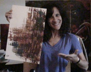 Cheryl Green holds an earth-toned abstract painting on white paper and smiles for the camera.