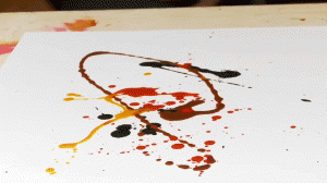 White paper with squirts and dots of red, yellow, and brown paint, and black ink.