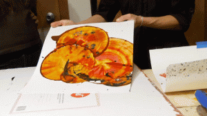 A white paper with red, yellow, brown, and black painted swirling spheres.