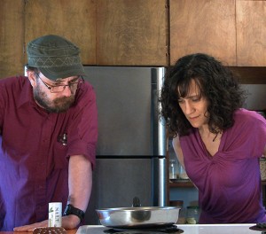 Cheryl and Bill stand at the stove staring intently at a saucepan, waiting for something to happen.