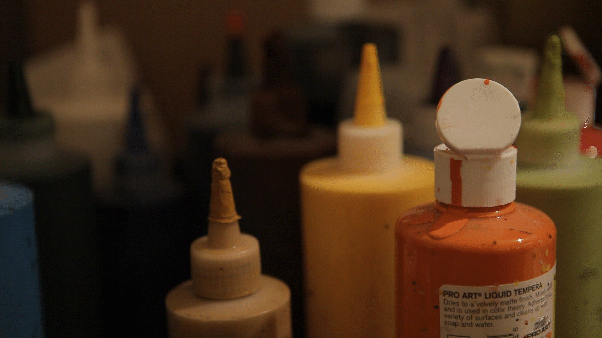 Paint bottles of blue, black, green, yellow, and orange with paint dripping from them.