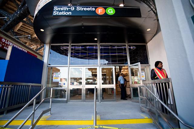 Entrance to the Smith-9th Street subway station for lines F and G. A short set of stairs leads up to doors with yellow "caution" tape. Stairs have bright yellow paint between them.
