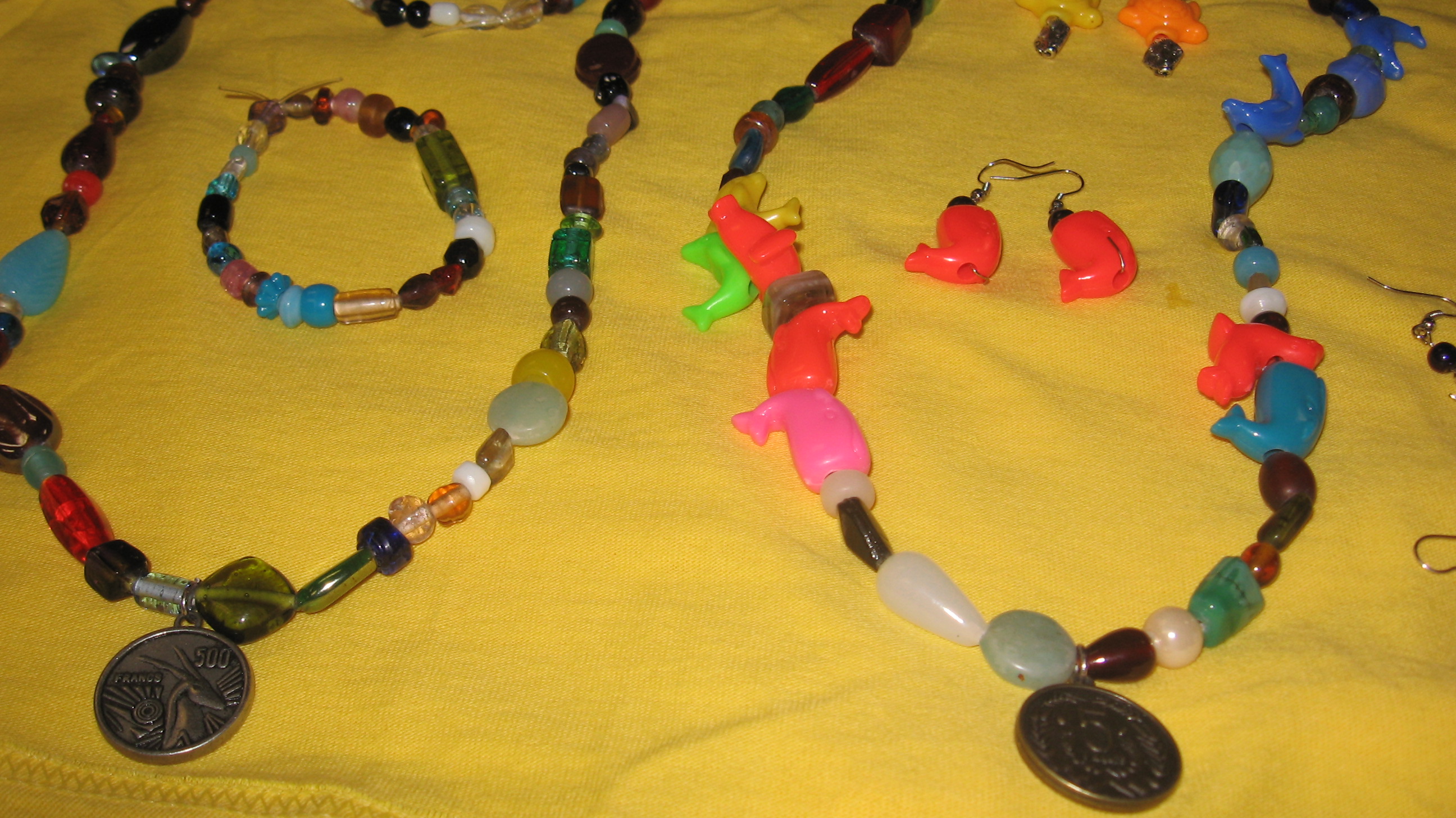 hand beaded jewelry Two beaded necklaces, a bracelet, and a set of earrings all handmade. Some colors are earth tones, and some are bright and vibrant. Pendants are foreign coins.