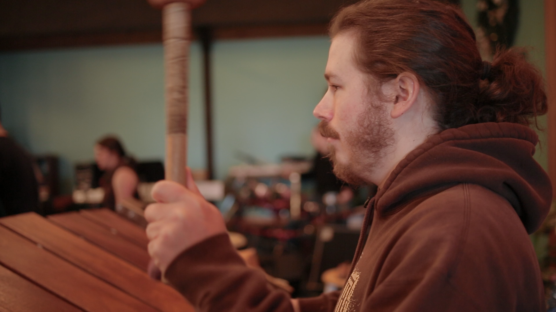 Brandon, now with beard and hair in a ponytail, plays a large marimba with thick mallets.