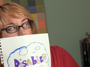 Caitlin holds a sign up that covers her chin and mouth. She looks off to the side. The sign says "Disabled" in alternating yellow and purple marker. It floats in a puffy, blue cloud, filled with more blue clouds and some blue birds.