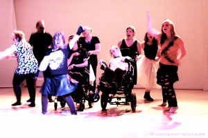 Nine dancers with and without disabilities onstage, wearing grungy, punk-inspired costumes strike poses at the end of a dance piece. Photo by Shannon Knight.