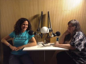 Two women sit at a table with studio microphones in front of them. Cheryl wears a Criptiques t-shirt, and Lavaun wears a black and white dress.