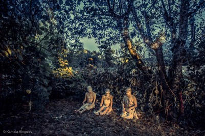 Three dancers, painted in white, sit among tall trees in a dreamlike image by Kamala Kingsley.