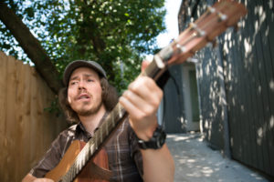 Brandon sits outside, playing guitar and singing.