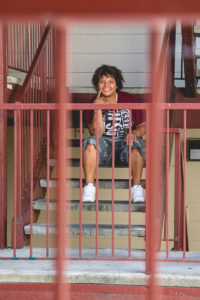 Dani sits on the steps of her apartment, smiling.