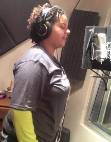 Dani Sanderson wears headphones and raps into a microphone in a recording studio.