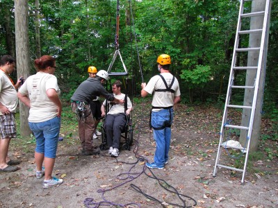 A man in a wheelchair is strapped into a safety harness getting ready for the zip line in the woods.