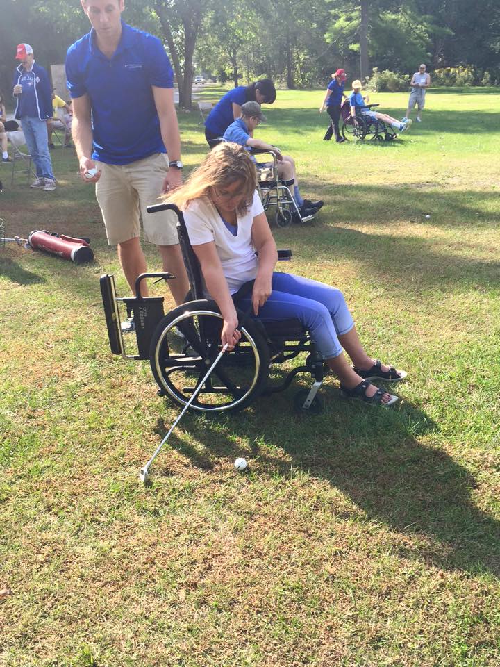 Three people in wheelchairs playing golf with staff nearby for support.
