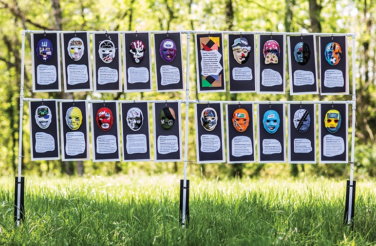 20 multi-colored, hand-decorated masks hang outside with a short story beneath each one.