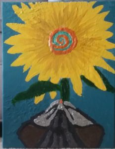 Thick, textured acrylic painting from above. A gray striped cat leans its head toward a frilly sunflower, its seeds a bright, orange spiral in the center.